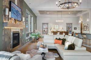 Living area with wood finished floors, a chandelier, a glass covered fireplace, and a tray ceiling
