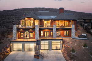 Back of house with a balcony, stairs, a garage, a chimney, and driveway