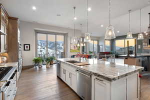 Kitchen with stainless steel appliances, a center island with sink, a mountain view, light stone counters, and hanging light fixtures