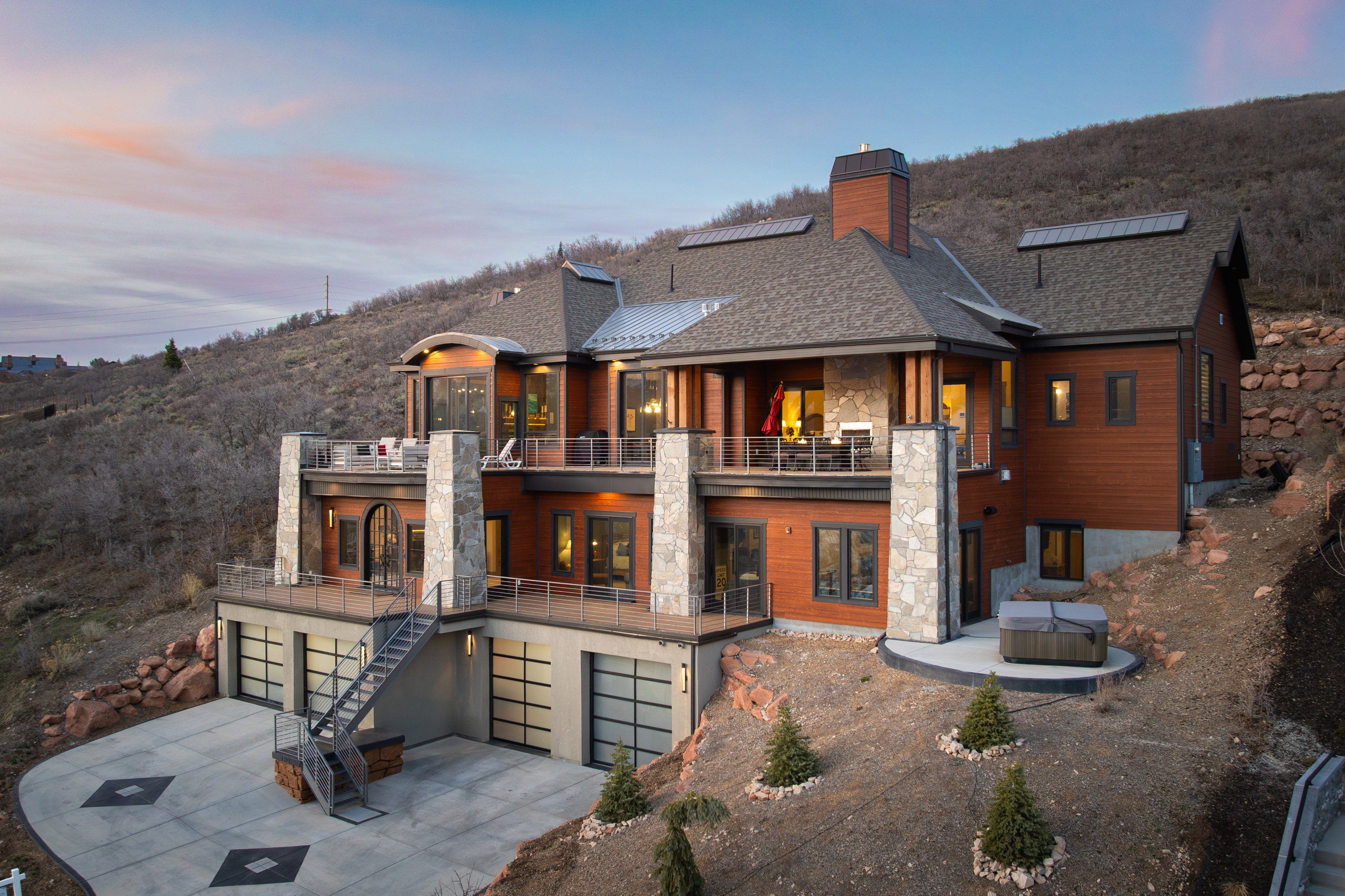 Back of property with a balcony, stone siding, a chimney, concrete driveway, and a garage