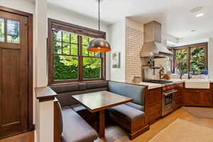 Kitchen with breakfast area, island exhaust hood, premium stove, light wood finished floors, and decorative backsplash