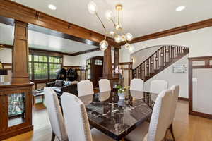 Dining area featuring decorative columns, arched walkways, crown molding, light wood finished floors, and a chandelier