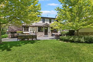 Rear view of house featuring stone siding, a patio, a lawn, and a chimney
