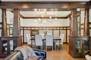 Dining area featuring decorative columns, wood finished floors, a chandelier, and ornamental molding