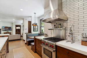 Kitchen with island range hood, premium range, light countertops, backsplash, and light wood finished floors