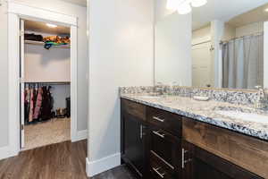 Full bathroom with wood finished floors, double vanity, and a walk in closet