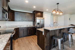 Kitchen with stainless steel appliances, light wood-style floors, dark brown cabinets, a textured ceiling, and recessed lighting