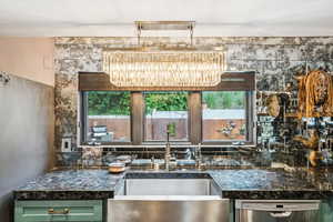 Kitchen with stainless steel dishwasher, a chandelier, green cabinetry, dark stone counters, and tasteful backsplash