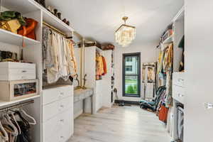 Walk in closet with light wood finished floors and a chandelier