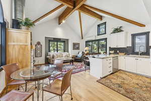Dining area with beam ceiling, light wood-style flooring, a wall mounted air conditioner, and high vaulted ceiling