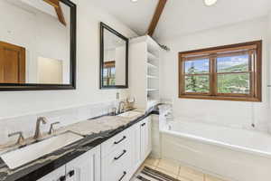 Full bath with double vanity, a bath, tile patterned flooring, beamed ceiling, and tasteful backsplash