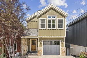 View of front facade with a garage, stone siding, board and batten siding, and roof with shingles