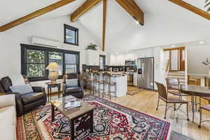 Living room with a wall mounted air conditioner, light wood finished floors, stairway, beamed ceiling, and high vaulted ceiling