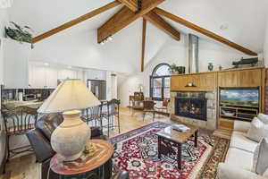 Living room featuring light wood-style flooring, beamed ceiling, high vaulted ceiling, and a fireplace