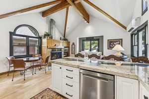Kitchen with dishwasher, beam ceiling, light wood-type flooring, a wall mounted air conditioner, and a stone fireplace