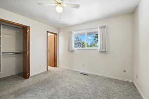 Unfurnished bedroom featuring carpet floors, a textured ceiling, a closet, and ceiling fan