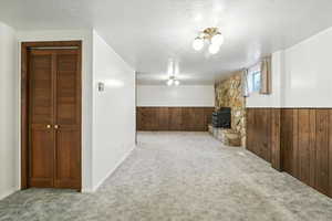 Unfurnished living room with wood walls, carpet, wainscoting, a textured ceiling, and a wood stove