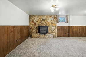 Unfurnished living room with wainscoting, wood walls, a textured ceiling, carpet, and heating unit