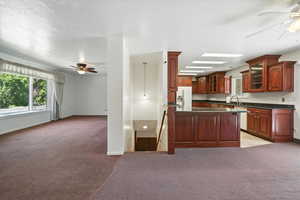 Kitchen featuring a ceiling fan, white refrigerator with ice dispenser, light carpet, dark countertops, and a textured ceiling