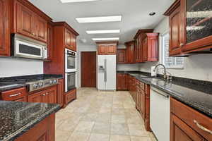 Kitchen featuring appliances with stainless steel finishes, dark stone counters, and glass insert cabinets