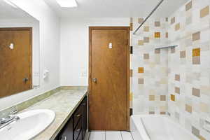 Bathroom featuring vanity, shower / bathtub combination, a textured ceiling, and tile patterned floors