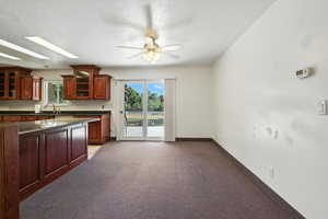 Kitchen with dark countertops, glass insert cabinets, a ceiling fan, dark brown cabinets, and a textured ceiling