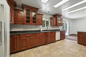 Kitchen featuring dishwasher, refrigerator with ice dispenser, dark countertops, glass insert cabinets, and light colored carpet
