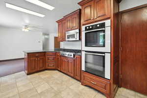 Kitchen featuring appliances with stainless steel finishes, a peninsula, ceiling fan, and light carpet