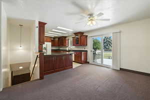 Kitchen with dark countertops, a peninsula, white fridge with ice dispenser, glass insert cabinets, and a ceiling fan