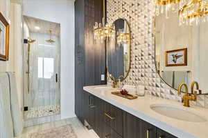 Bathroom with a chandelier, a shower stall, double vanity, and decorative backsplash