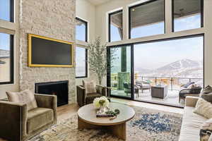 Living room featuring wood finished floors, plenty of natural light, a stone fireplace, and a towering ceiling