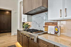 Kitchen with premium range hood, tasteful backsplash, light stone counters, light wood finished floors, and stainless steel gas cooktop