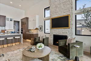 Living area with a high ceiling, light wood-style flooring, and a stone fireplace