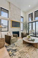 Living area with a stone fireplace, wood finished floors, recessed lighting, and a high ceiling