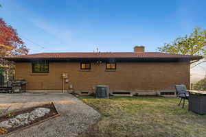 Rear view of house with a chimney, a lawn, and brick siding
