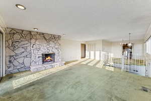 Unfurnished living room with carpet floors, a fireplace, a chandelier, and a textured ceiling