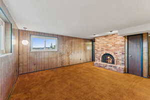 Unfurnished living room featuring a textured ceiling, carpet floors, wood walls, and a brick fireplace
