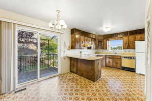 Kitchen featuring freestanding refrigerator, dishwashing machine, a peninsula, light countertops, and under cabinet range hood
