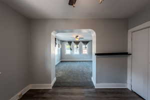 Empty room with arched walkways, ceiling fan, and dark wood-style floors