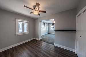 Empty room with a ceiling fan, arched walkways, dark wood-type flooring, and a textured ceiling