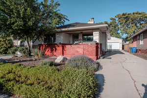 View of front of home featuring an outbuilding, a chimney, brick siding, a detached garage, and stucco siding
