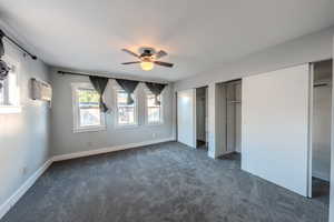 Unfurnished bedroom featuring a wall unit AC, dark carpet, multiple closets, and a ceiling fan