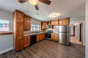 Kitchen with appliances with stainless steel finishes, open shelves, a textured ceiling, decorative backsplash, and dark wood finished floors