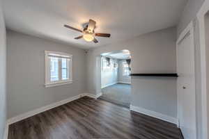 Empty room featuring ceiling fan, arched walkways, and dark wood-style floors