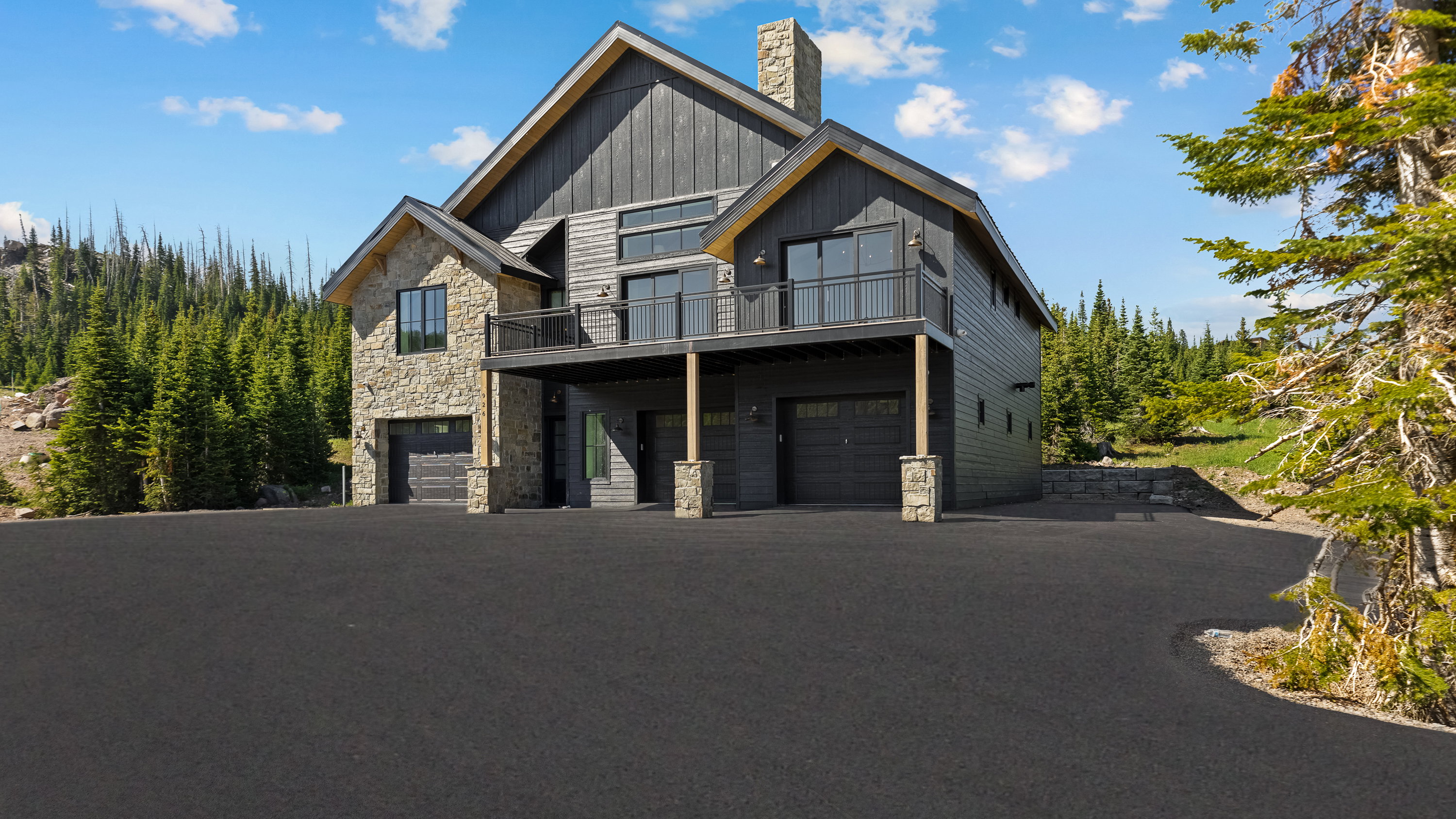 View of front of property with stone siding, a garage, a chimney, board and batten siding, and a balcony
