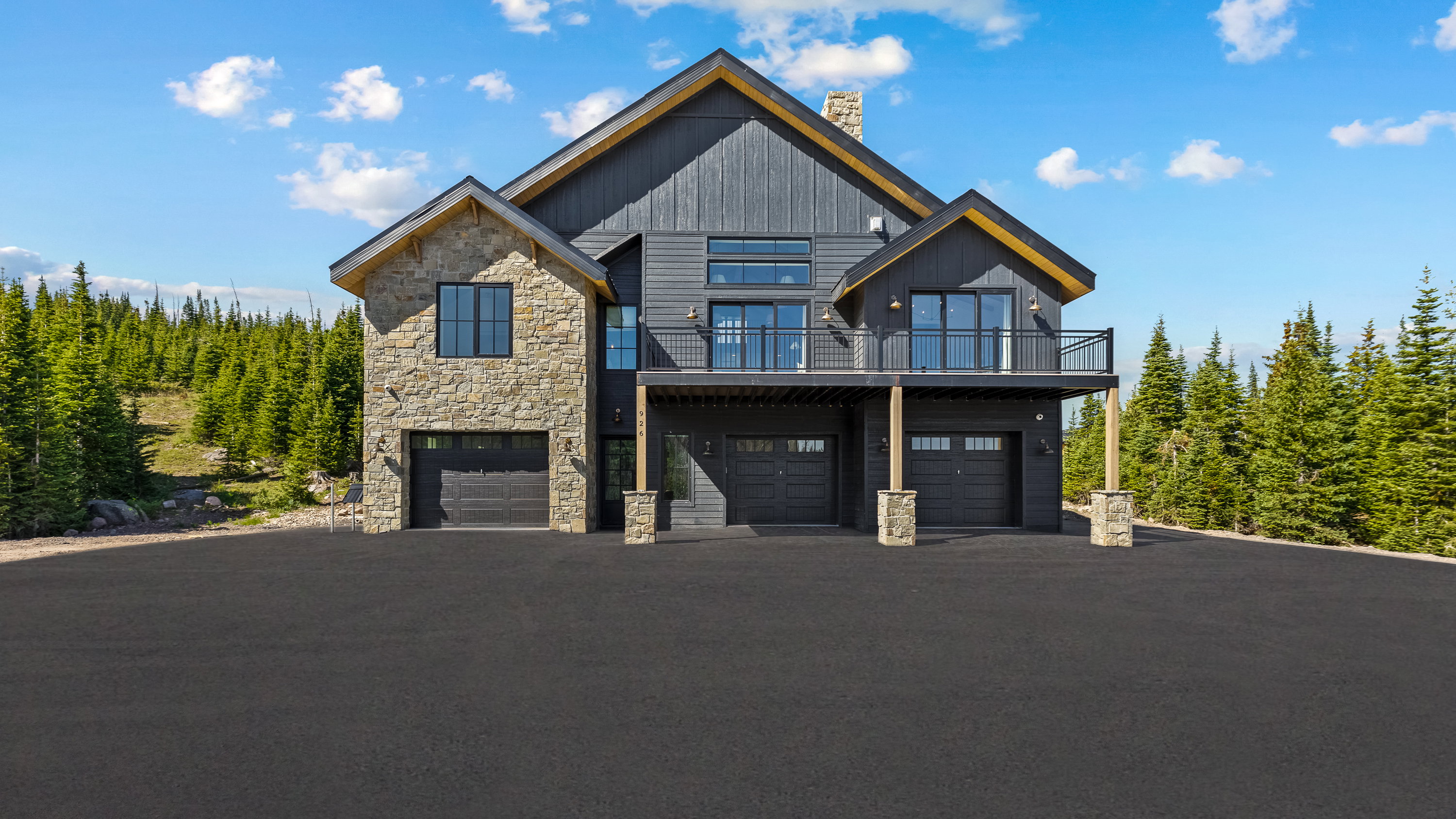 View of front of property featuring stone siding, a chimney, an attached garage, a balcony, and asphalt driveway