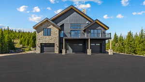 View of front of property featuring stone siding, a chimney, an attached garage, a balcony, and asphalt driveway