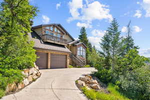 View of front facade with a balcony, driveway, a garage, stone siding, and stairs