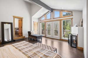 Bedroom with access to exterior, wood finished floors, a glass covered fireplace, beam ceiling, and high vaulted ceiling