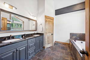 Bathroom with double vanity, a relaxing tiled tub, and stone finish flooring